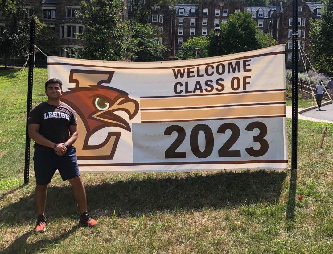 Josue Quintero standing in front of a sign that says Welcome Class of 2023.