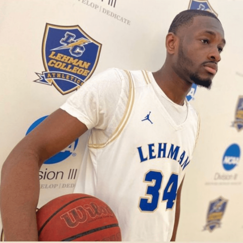 student wearing a sports jersey and basketball poses in front of Lehman College signage for CollegeBound Month celebrations