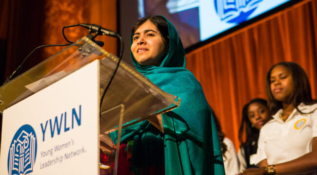 Malala stands at a podium and speaks to guests at Empower Breakfast.