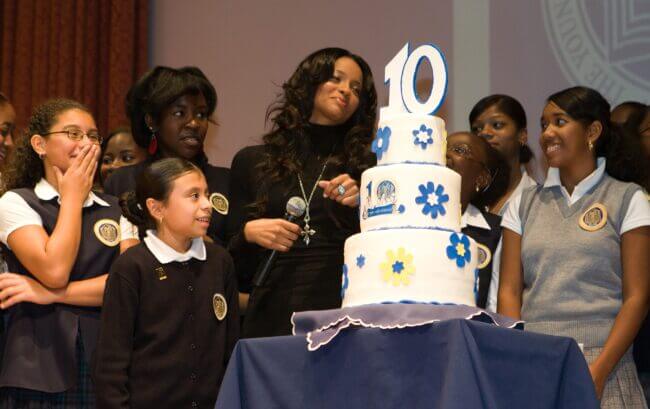 TYWLS students and Ciara stand around a three-tiered cake with number 10 topper to celebrate the organization's 10-year anniversary.