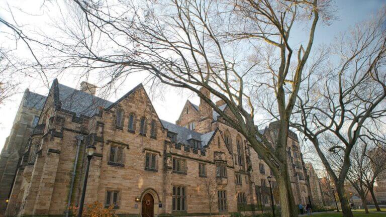 There is an old brick building standing against a cloudy sky and bare tree. The building is presumed to be on an Ivy League school campus.