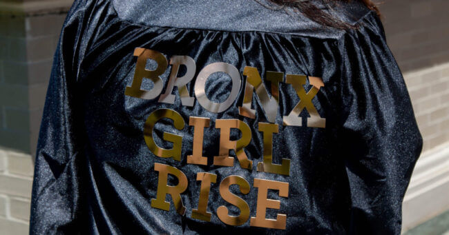 A graduate's gown has "Bronx Girl Rise" written on the back in bold gold letters.
