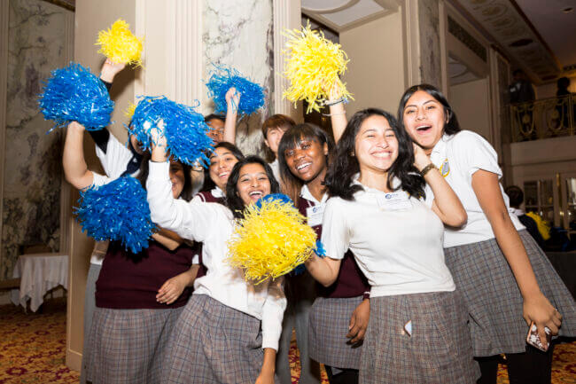 TYWLS students are cheering and shaking blue and yellow pom poms.
