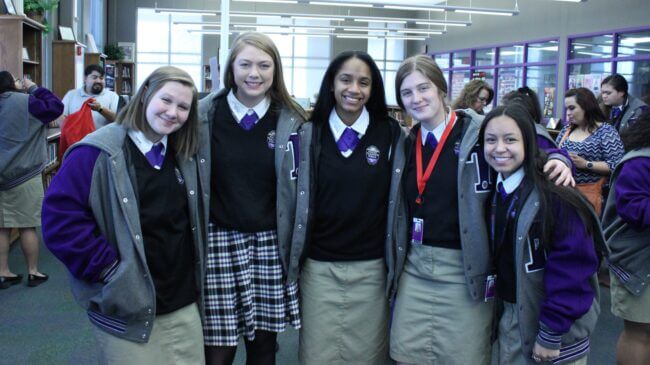 Five students are wearing their letter jackets and school uniforms. They are smiling for the camera.