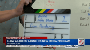 This is a screenshot from a new feature about GLOW Academy. A person is holding a clapperboard that says 'Digital Media Studio' Take 1 GLOW Academy.