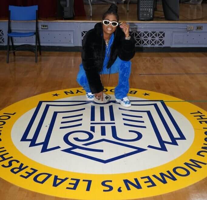Hoodcelebrityy visited TYWLS Brooklyn and poses for a picture kneeling on top of the TYWLS logo on the gym floor.