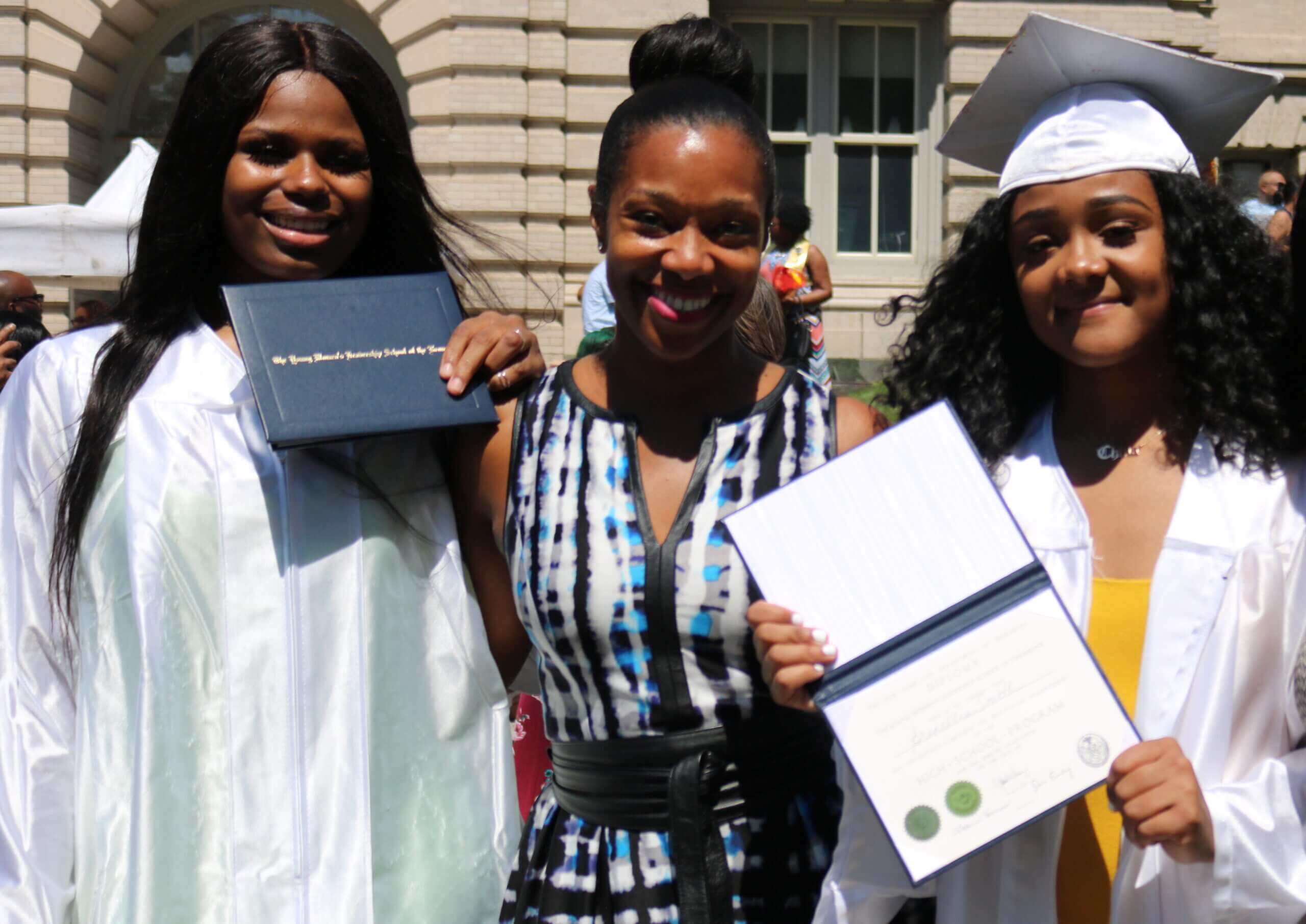CEO Yolonda Marshall stands in between two graduates from The Young Women's Leadership School of the Bronx. The graduates are holding up their diplomas.