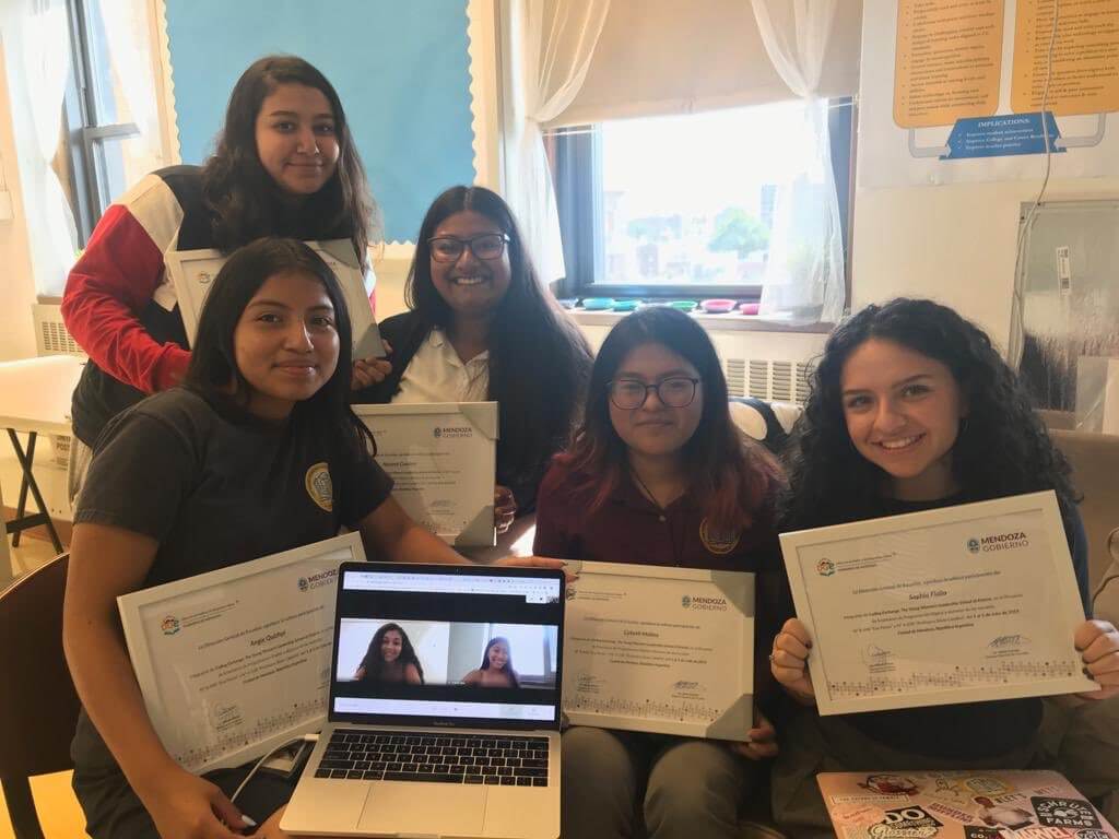 Michelle with her Coding Exchange peers. They are holding up certificates. There is a laptop in the middle of the group with two other members on the screen. 