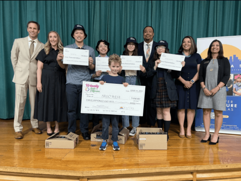 A group of students and Amazon reps stand together. Students are holding up novelty giant checks to represent their scholarships.