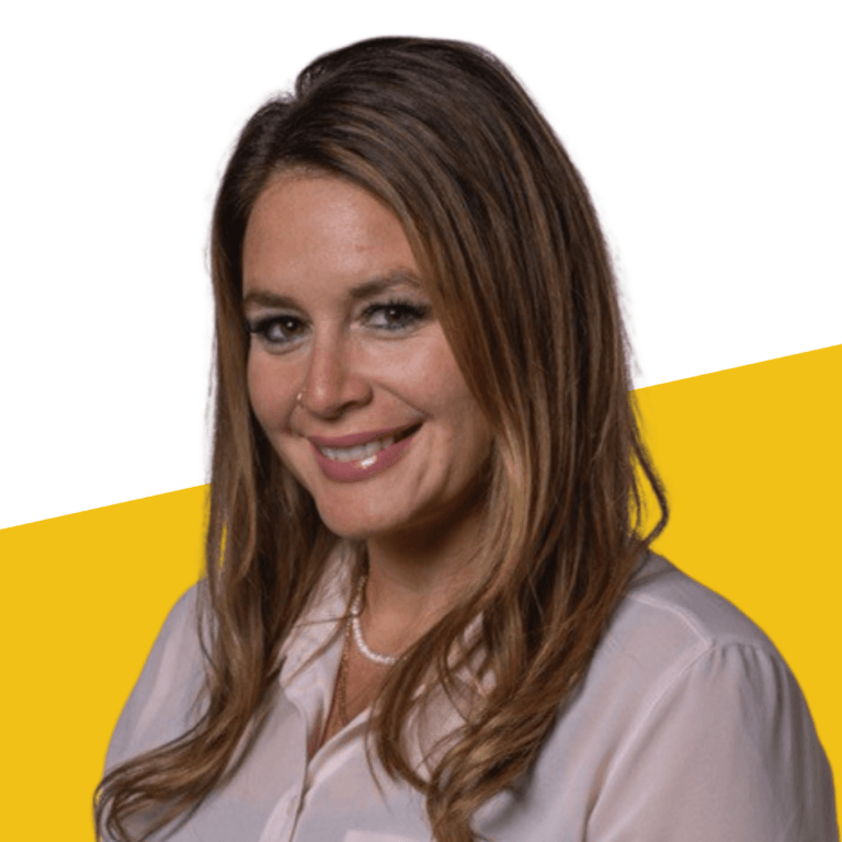 Woman with long brown hair wearing a light pink blouse and a pearl necklace, smiling in front of a white and yellow background.