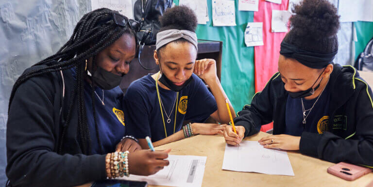 Three students are sitting at a table and working together on assignments.