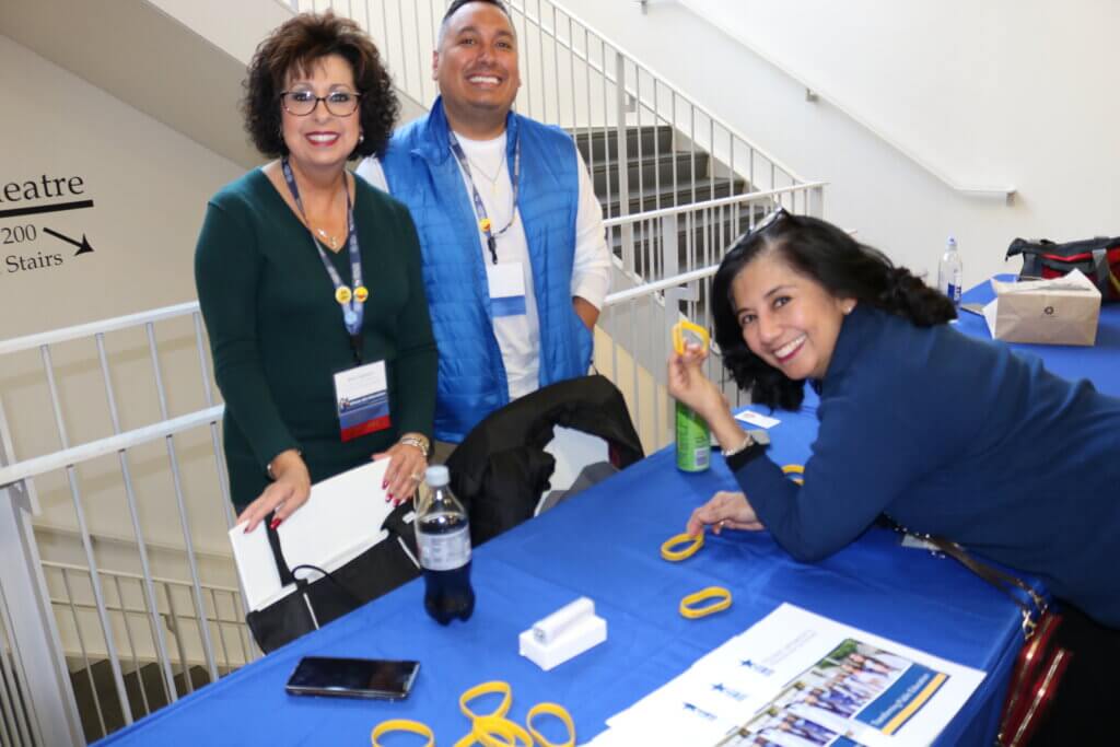 Three YWPN team members smile as they stand together by their exhibitor table