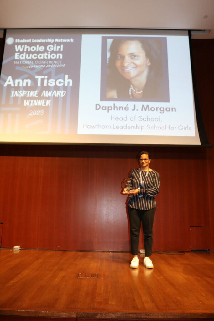 Daphne Morgan on stage holding her award with "Ann Tisch Inspire Award" on screen behind her