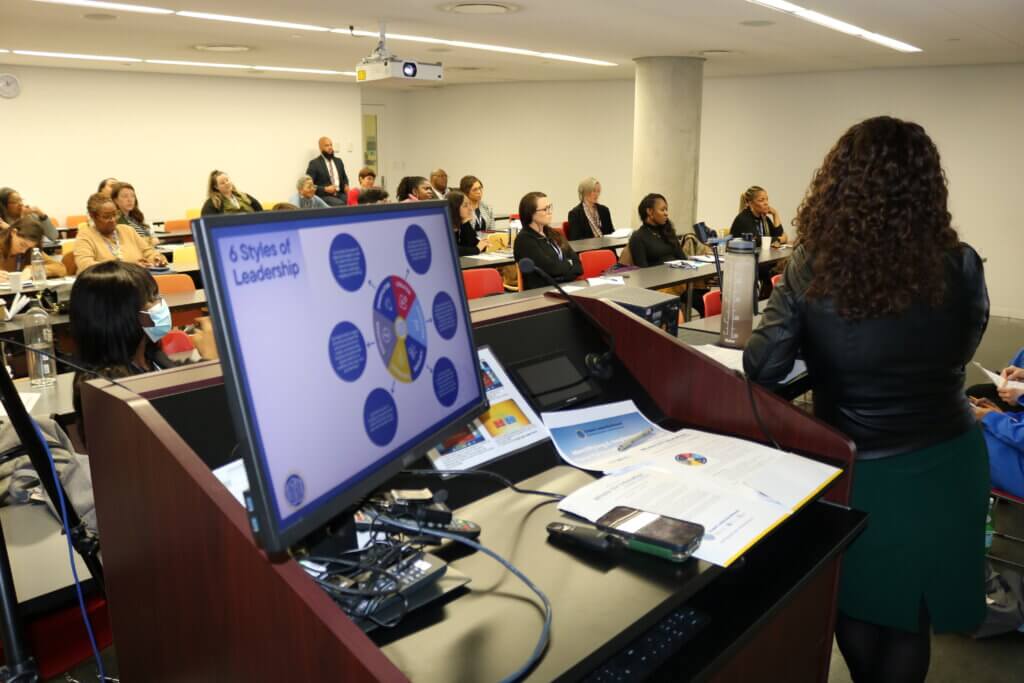A group of attendees sit in a classroom with a projector screen reading "6 styles of leadership" in the forefront