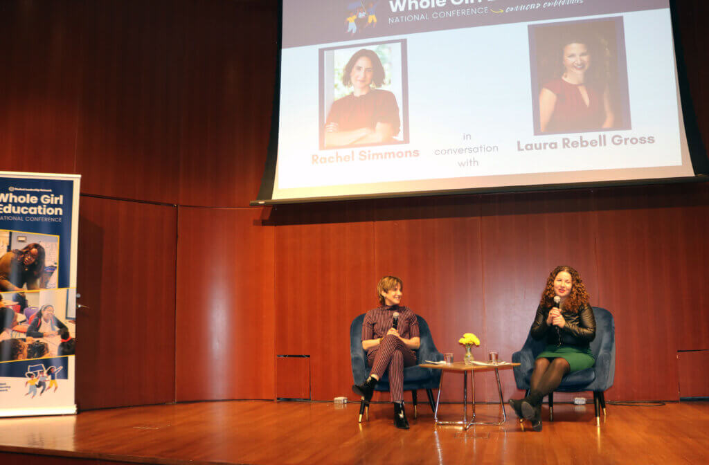 Rachel Simmons and Laura Rebell Gross sit on chairs on stage with a banner reading "Whole Girl Education"