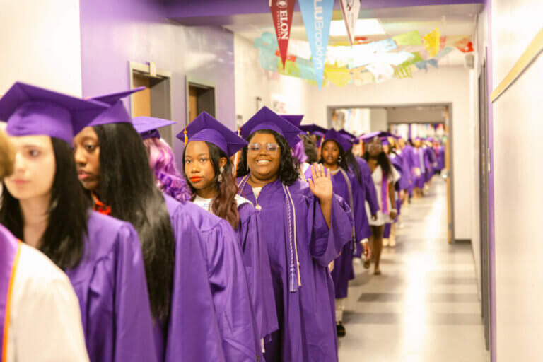 Girls in purple graduation caps and gowns line up in hallway