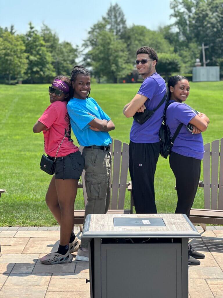 A director of college counseling and her students pose in front of a college campus lawn.