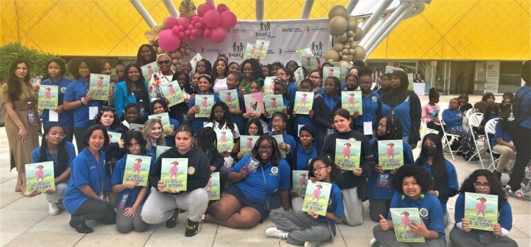 Group of students hold up picture books in front of a museum.