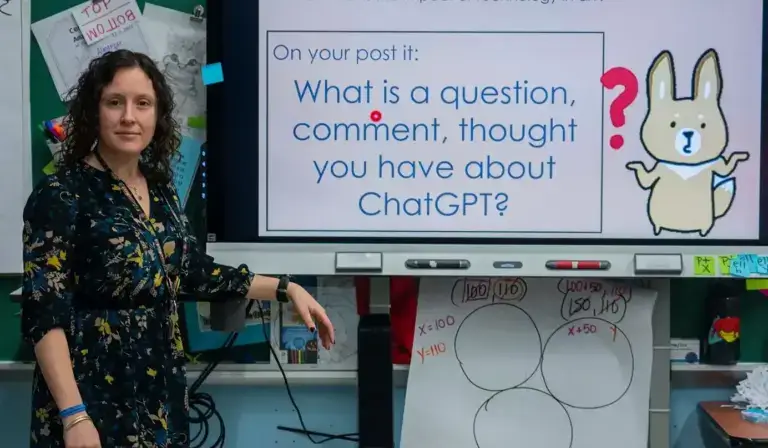 Teacher stands in front of a smartboard with a presentation about ChatGBT.