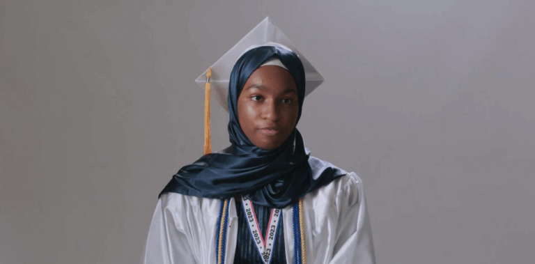 Student in headscarf, graduation cap, and gown wears a medal on ribbon around her neck