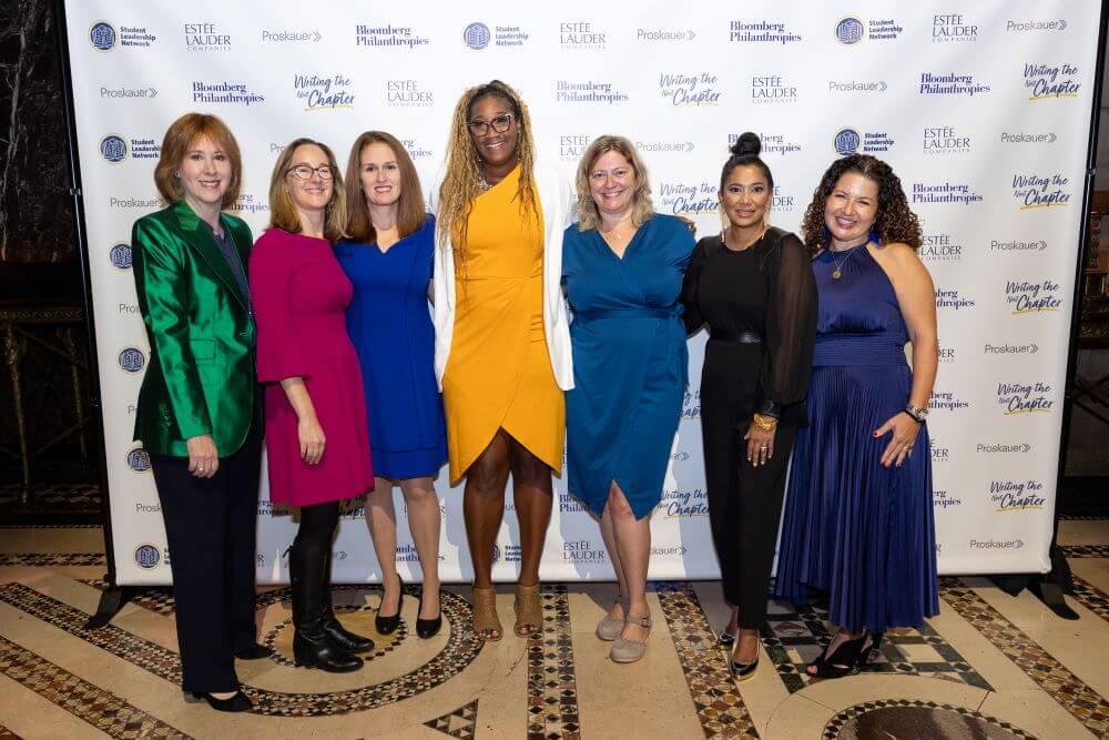 Principals of The Young Women's Leadership Schools, Ann Tisch, and Laura Rebell Gross pose for photo in front of Student Leadership Network backdrop