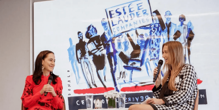 Two women company executives talk on stage with microphones in hand