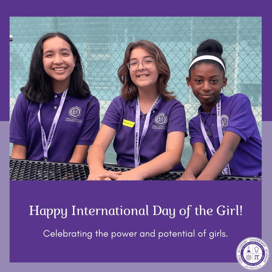 Three girls in school uniforms sit at table, with text on bottom "Happy International Day of the Girl! Celebrating the Power and Potential of girls."