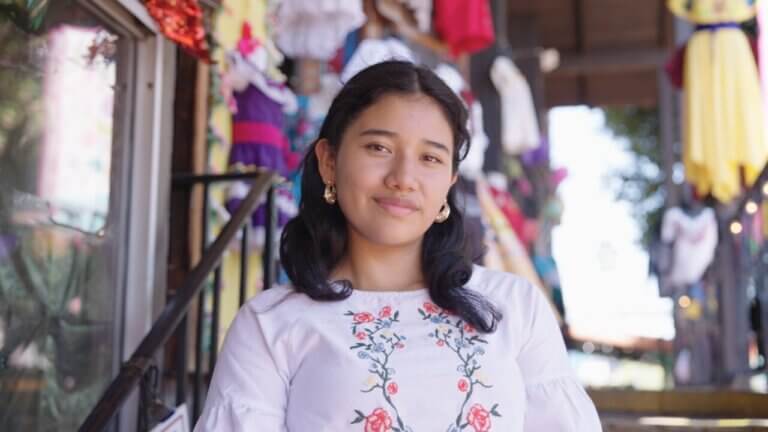 Student wearing earrings and a shirt with a floral motif smiles confidently at the camera