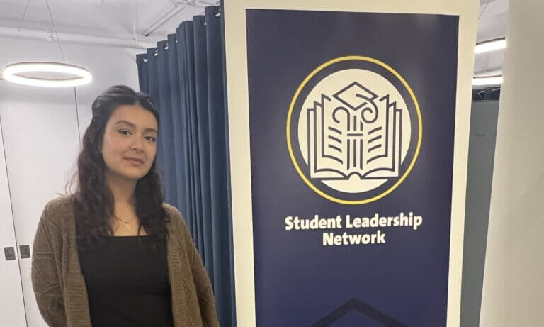 Young woman stands next to a banner with Student Leadership Network logo and crest