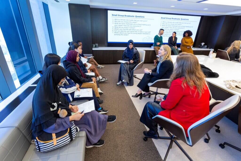 Group of seven students and two adults gather in a seated circle to talk