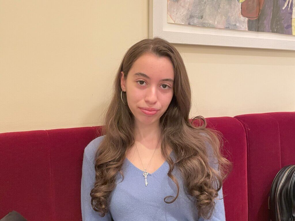 Young woman with long hair and hoop earrings is seated at a bench, facing the camera