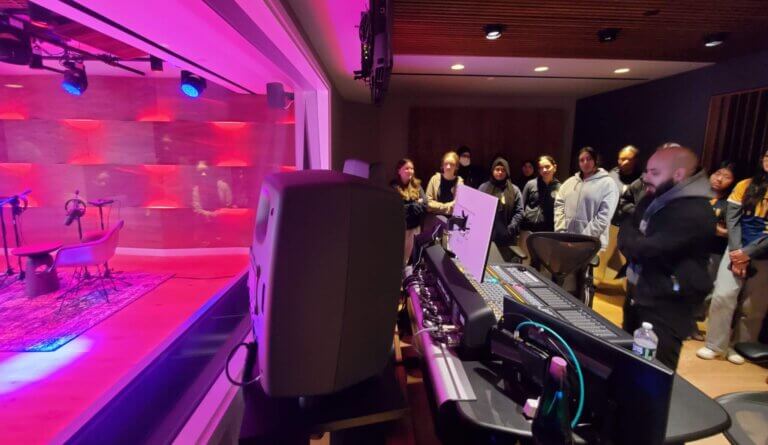 Sony staff member leads tour of sound studio with students. Recording studio is lit up in pink on the left.