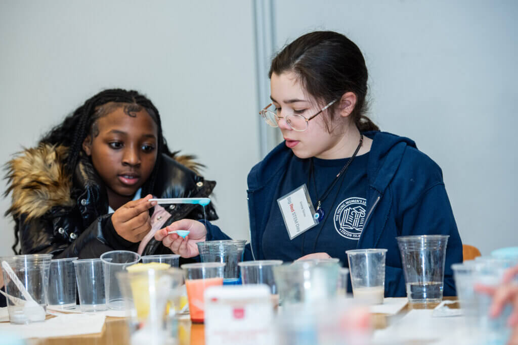Two students measure out a blue liquid into plastic cups