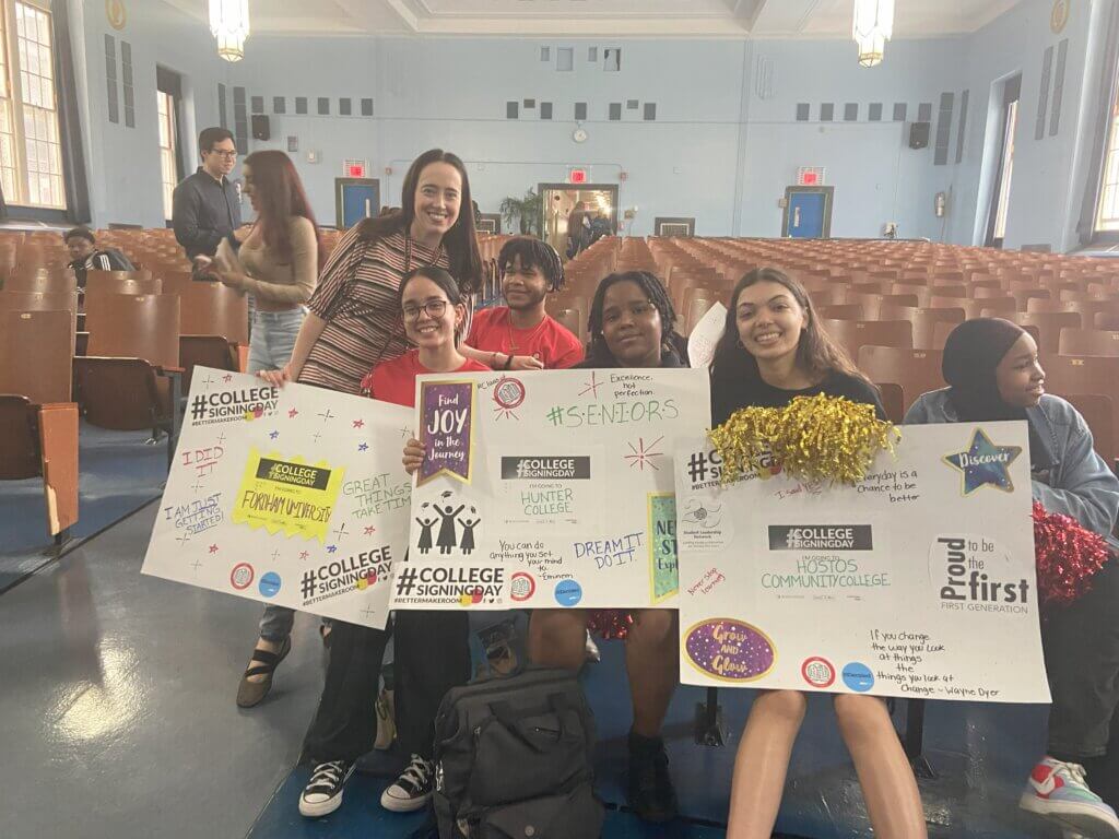 Adult and students hold up college acceptance posters inside auditorium
