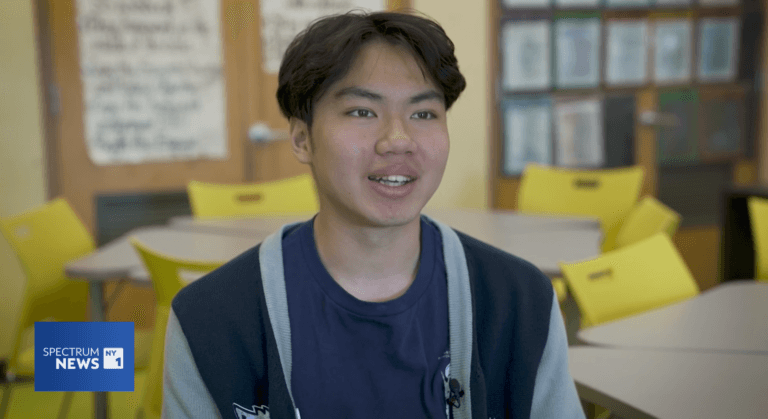 High school senior wears a varsity jacket in the classroom and smiles at camera