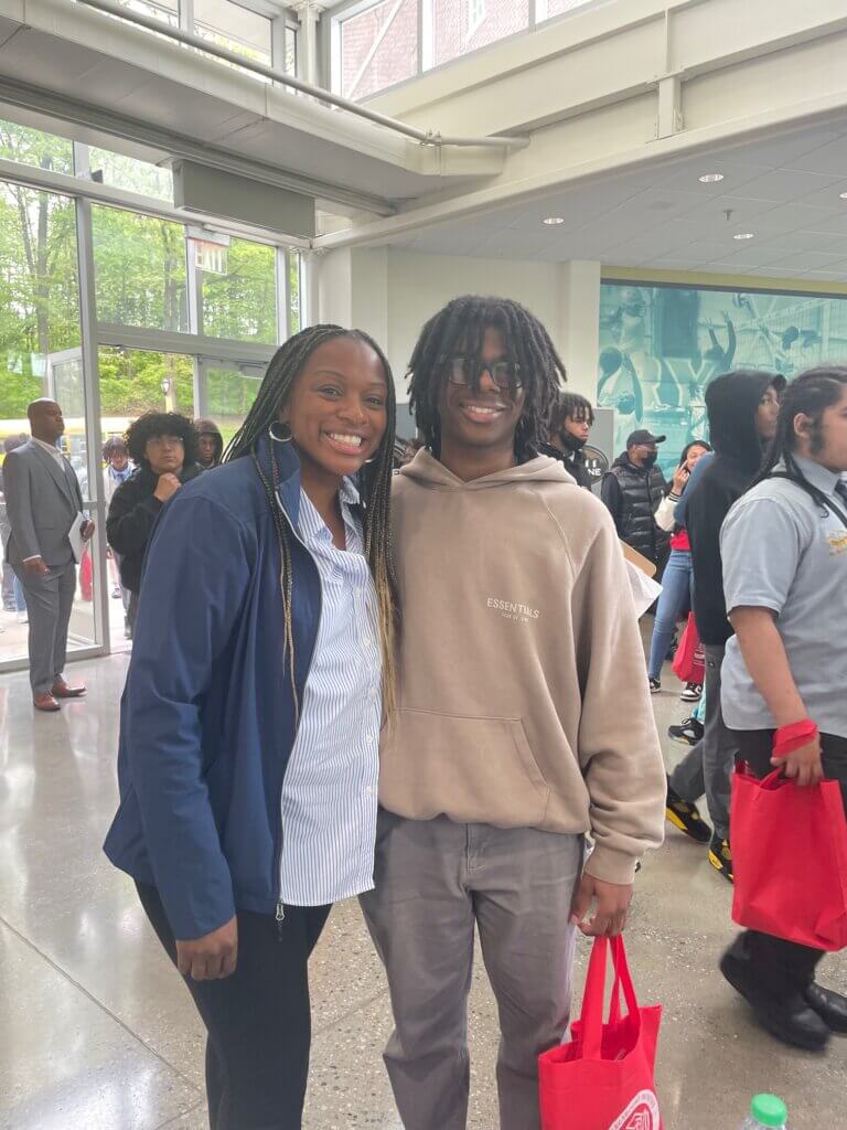 Staff member and student holding a red CBI tote bag smile at the camera