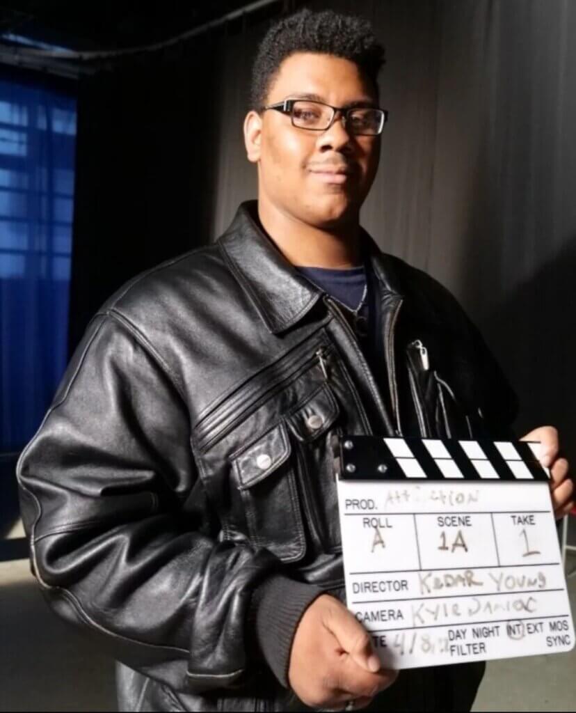 Young man in glasses and leather jacket holds up a director's clapboard