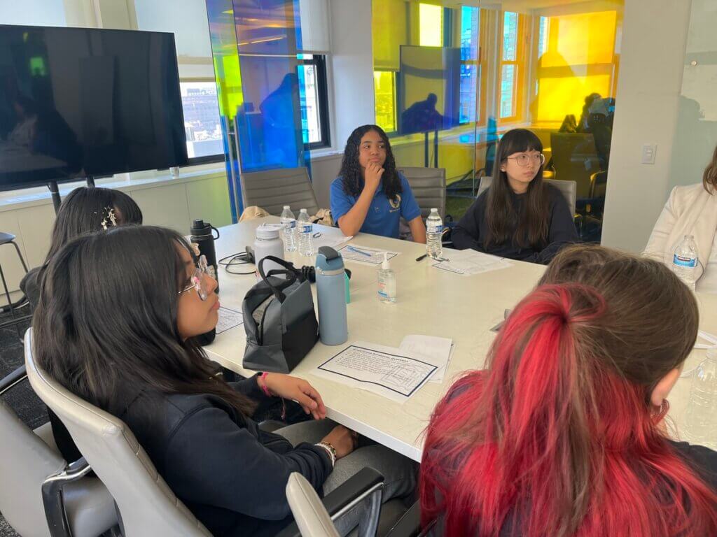 Five middle school students sit at a large conference table