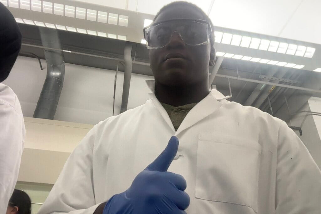 Young man wearing science goggles and a lab coat gives a thumbs up sign