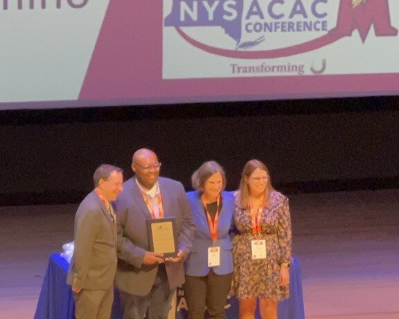 Rob Robinson holds award plaque on stage of New York State Association for College Admission Counseling conference