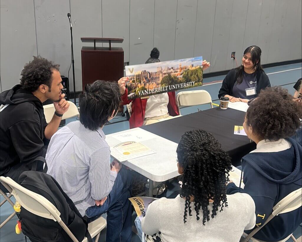 College representative is seated with students around a table with college materials