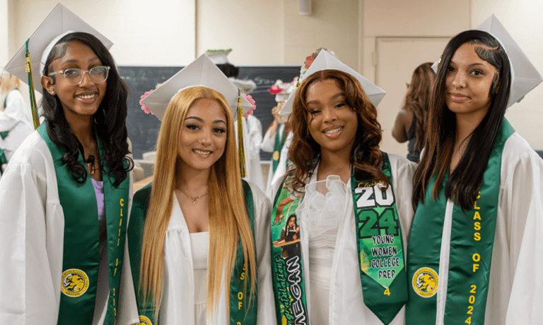 Four young women pose in white graduation caps and gowns and green graduation stoles