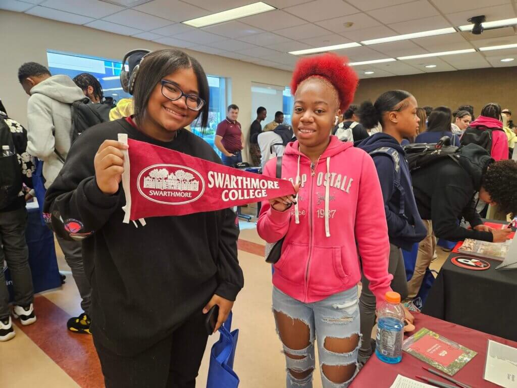 Two female students hold up a Swarthmore College pennant while navigating college fairs at school