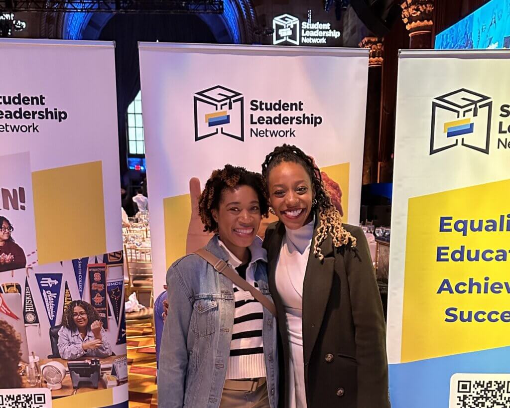 Two young women pose for photo in front of event banners