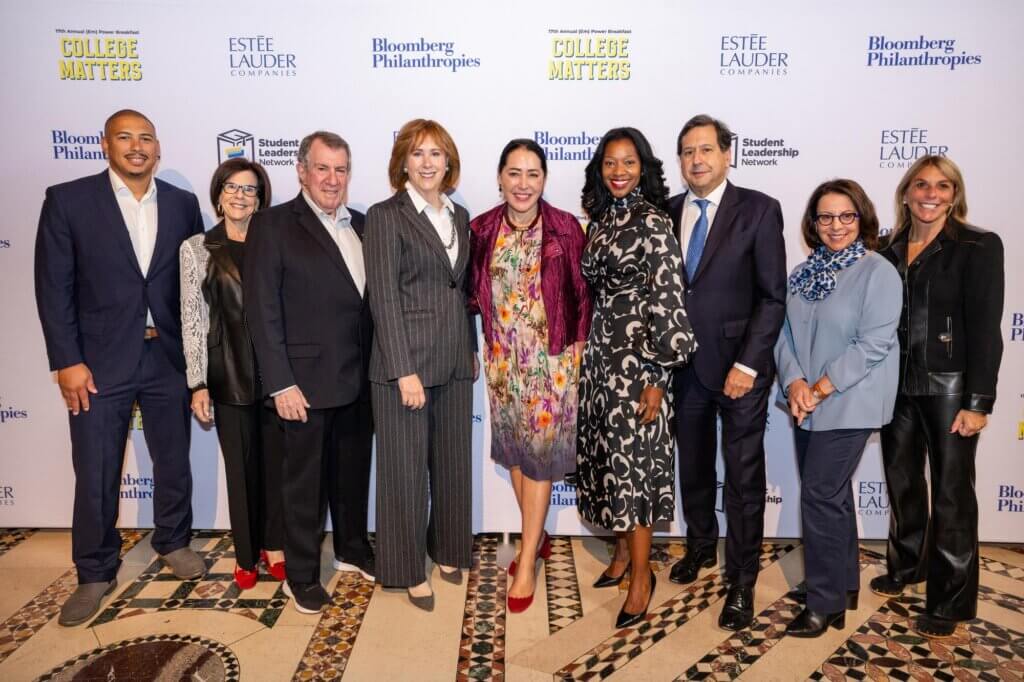 Board members in professional and festive attire pose for photo in front of event backdrop