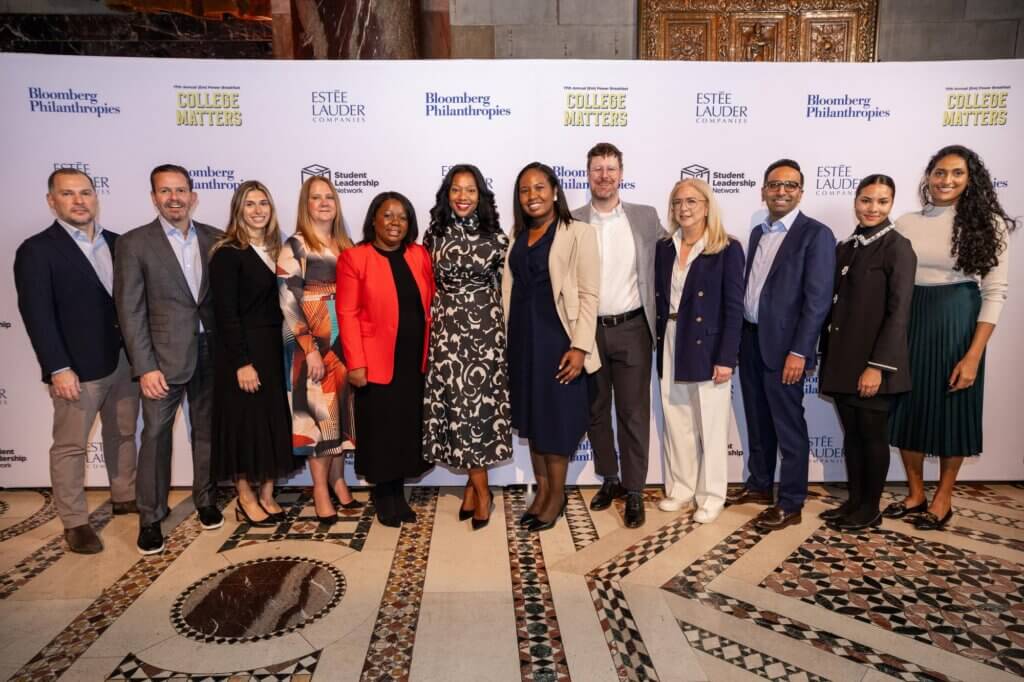 Guests in professional and festive attire pose for photo in front of event backdrop