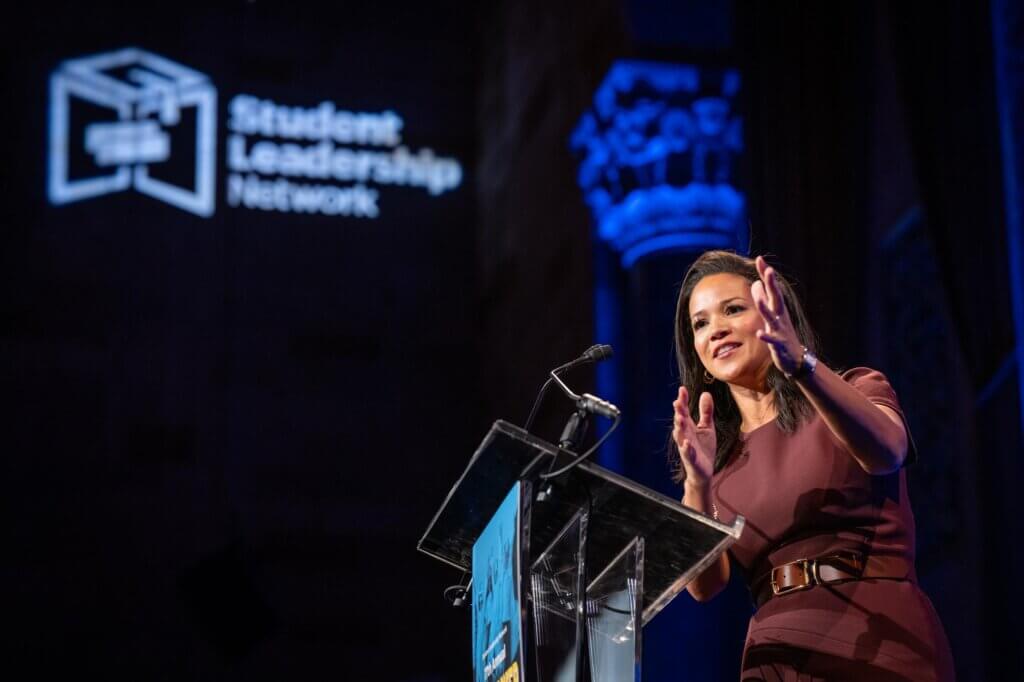 Laura Jarrett speaks at podium with arms gesturing to her left