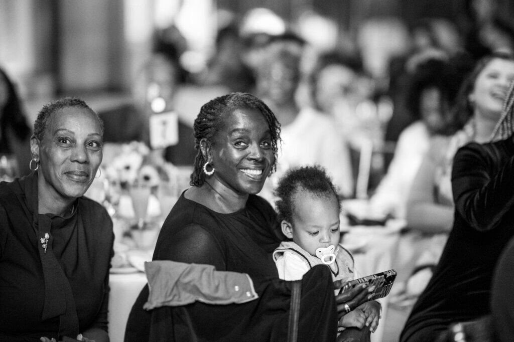 Proud family in audience, including a toddler, looks to the stage