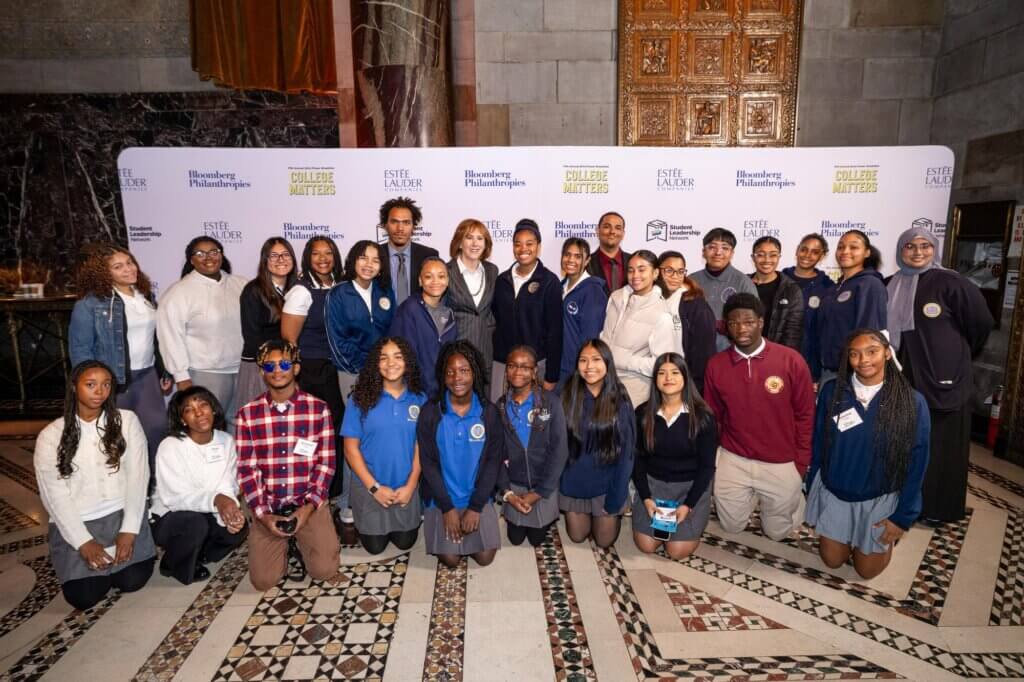Ann Tisch and students gather for photo in front of event backdrop