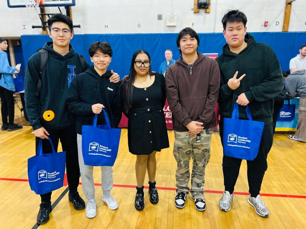 College counselor and four students pose for photo at college fair in gymnasium